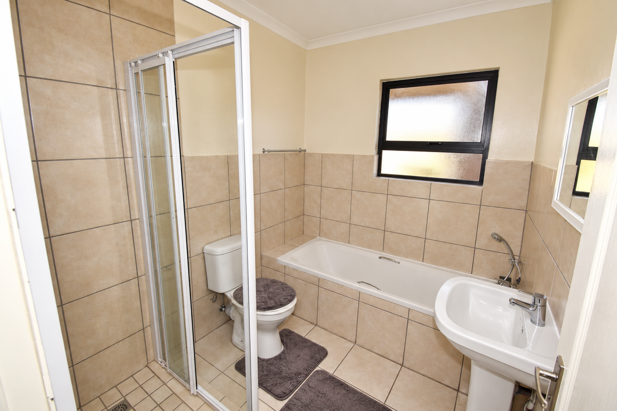 A functional bathroom featuring a shower enclosure, bathtub, pedestal basin, and toilet with neutral wall and floor tiling.