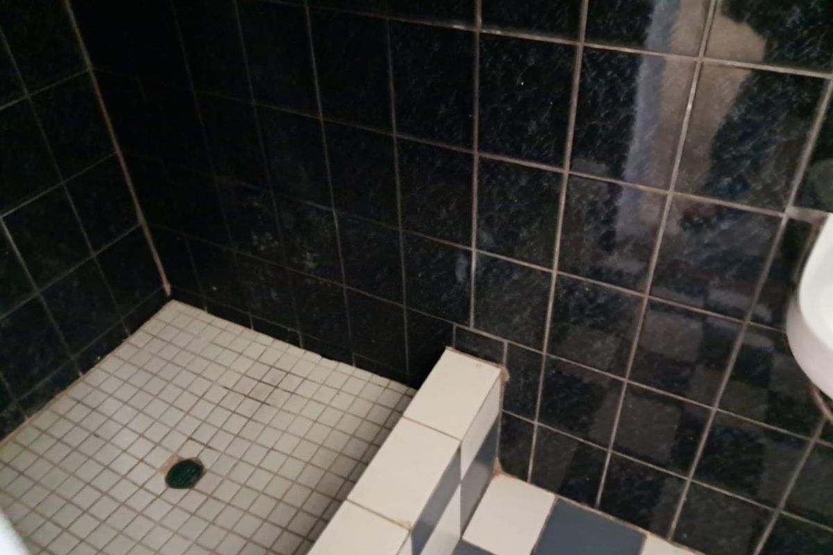 A close-up view of a shower area featuring dark wall tiles and a tiled shower curb, showing signs of wear in the grout.