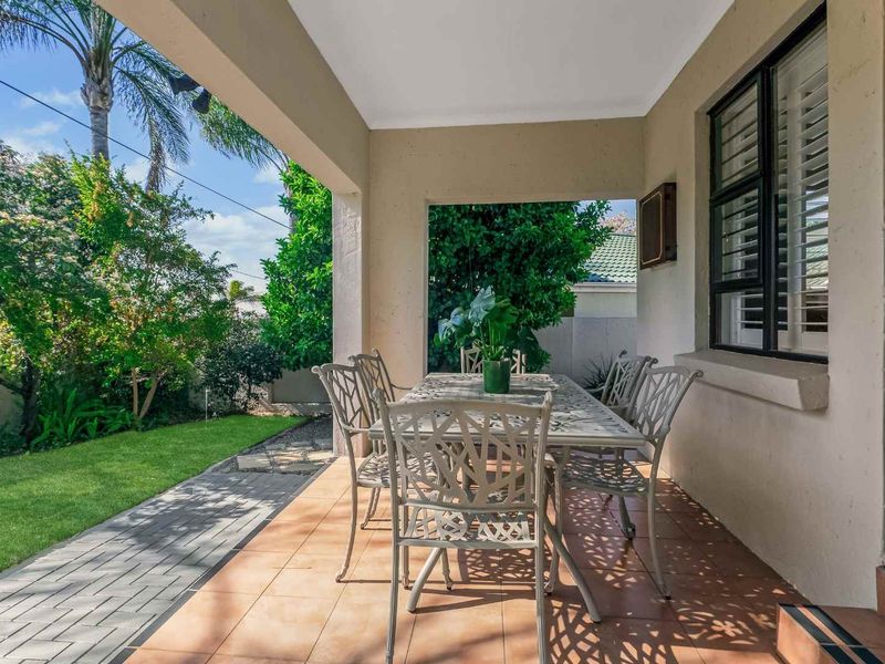 A well-maintained covered patio featuring tiled flooring and direct access to a landscaped garden area, perfect for outdoor dining and relaxation.