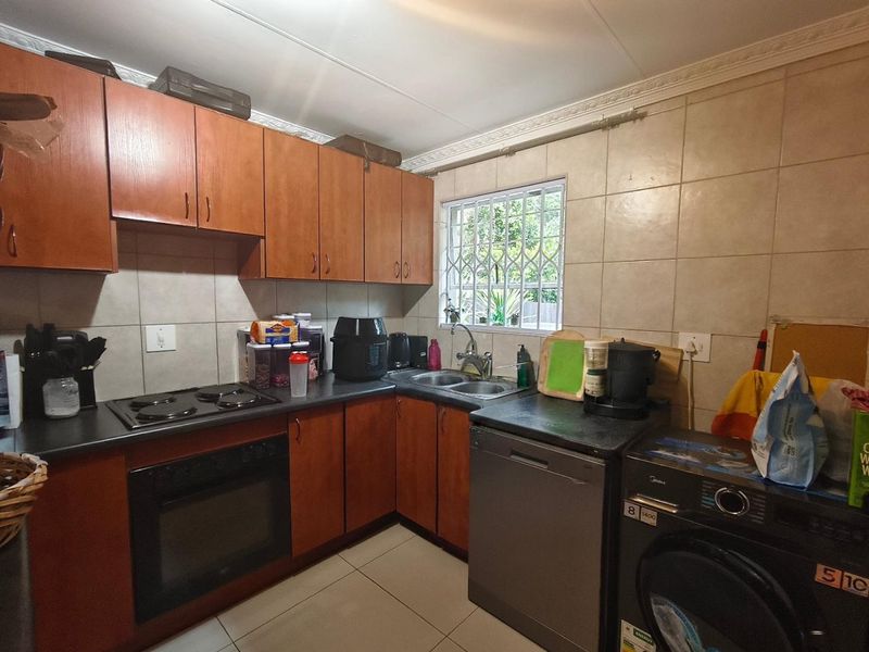 Functional kitchen featuring wood-finish cabinetry, dark laminate countertops, tiled backsplash, and integrated cooking appliances with a window overlooking the exterior.