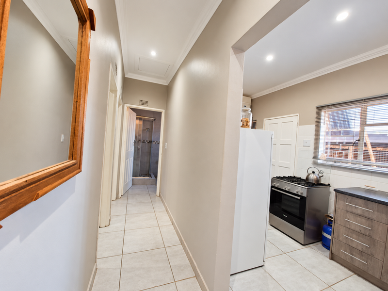 An open-plan view showing a tiled hallway leading to a bathroom and a functional kitchen area with modern cabinetry and a gas stove.