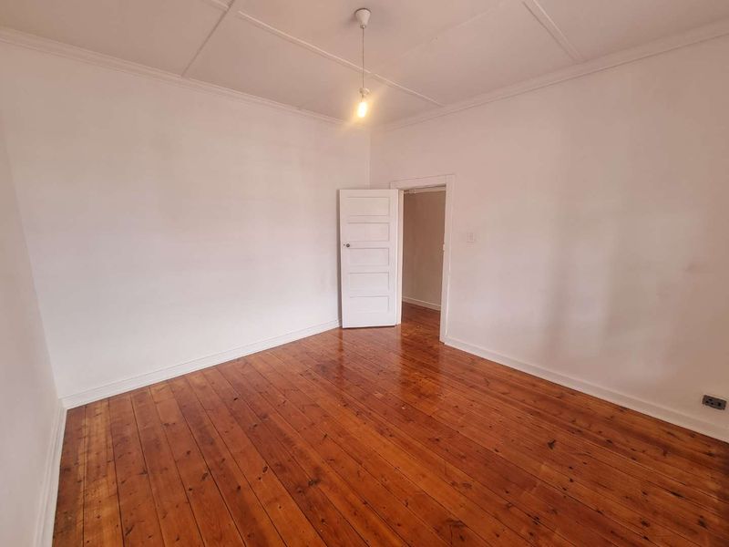 A vacant bedroom featuring polished timber flooring, white walls, and a classic panelled door, offering a clean canvas for interior design.