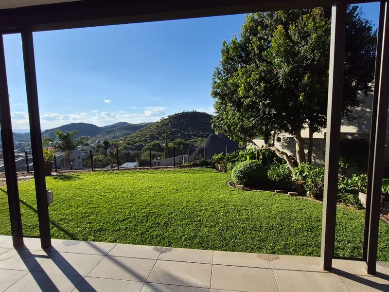 A covered patio area overlooking a well-maintained garden with expansive mountain and landscape views.