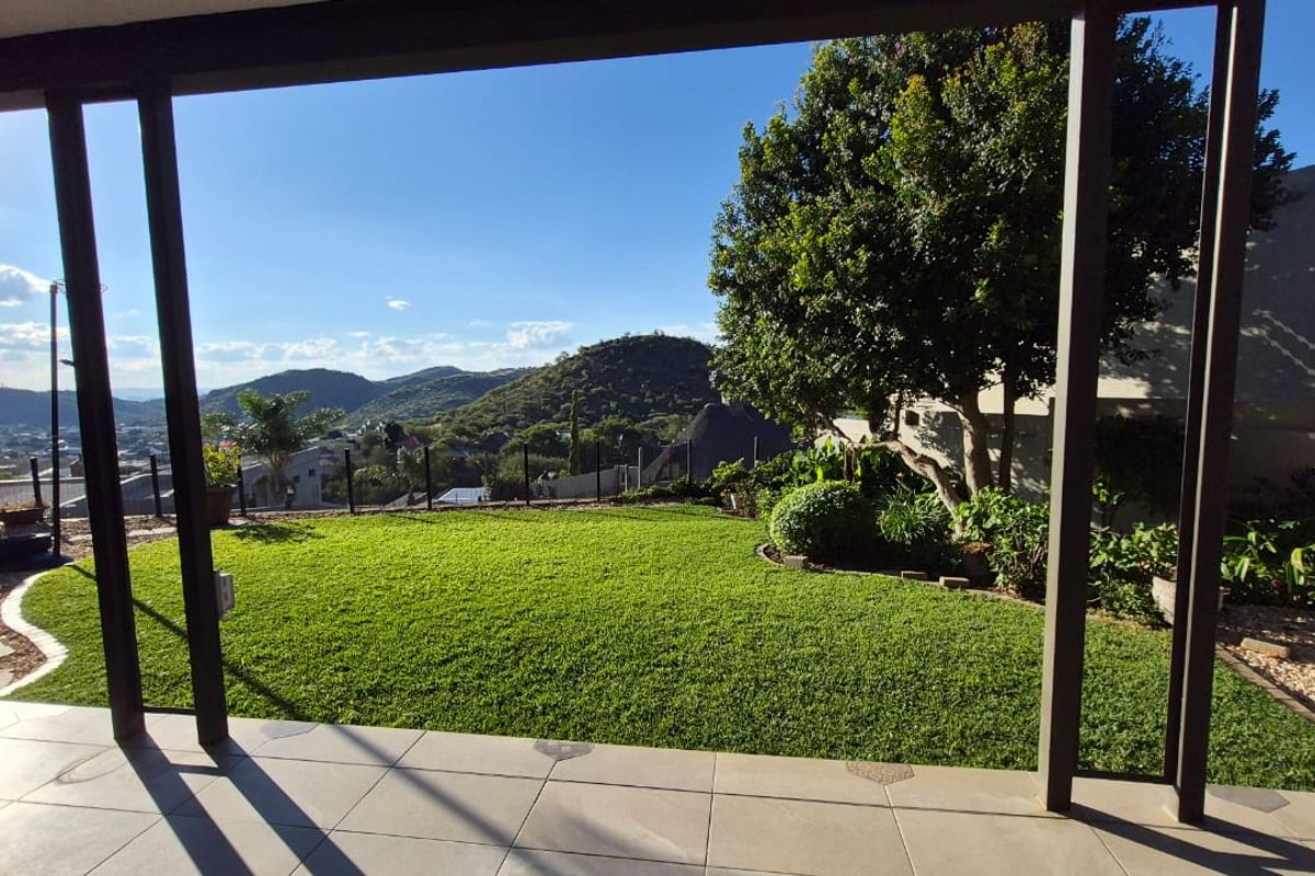 A covered patio area overlooking a well-maintained garden with expansive mountain and landscape views.