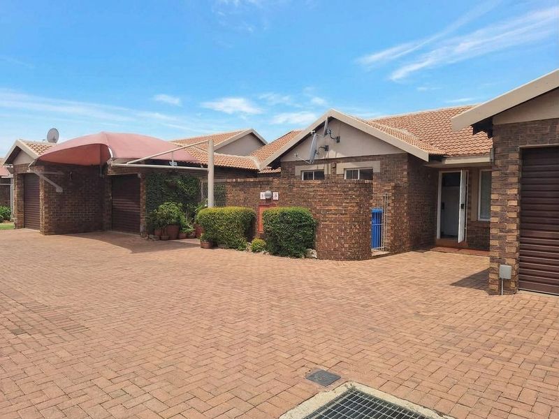 Front exterior view of a townhouse featuring a paved driveway, brick facade, tiled roof, and garage access.