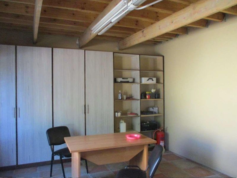 Functional office space featuring built-in cabinetry, open shelving, exposed timber ceiling beams, and durable tiled flooring.