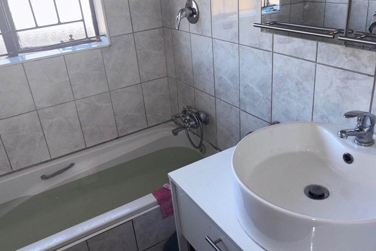 A functional bathroom featuring a tiled bathtub with shower mixer, a modern vessel sink vanity, and a window with security bars.