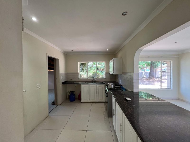 A functional kitchen featuring granite countertops, white cabinetry, a gas stove, and a breakfast bar, with tiled flooring and natural light.