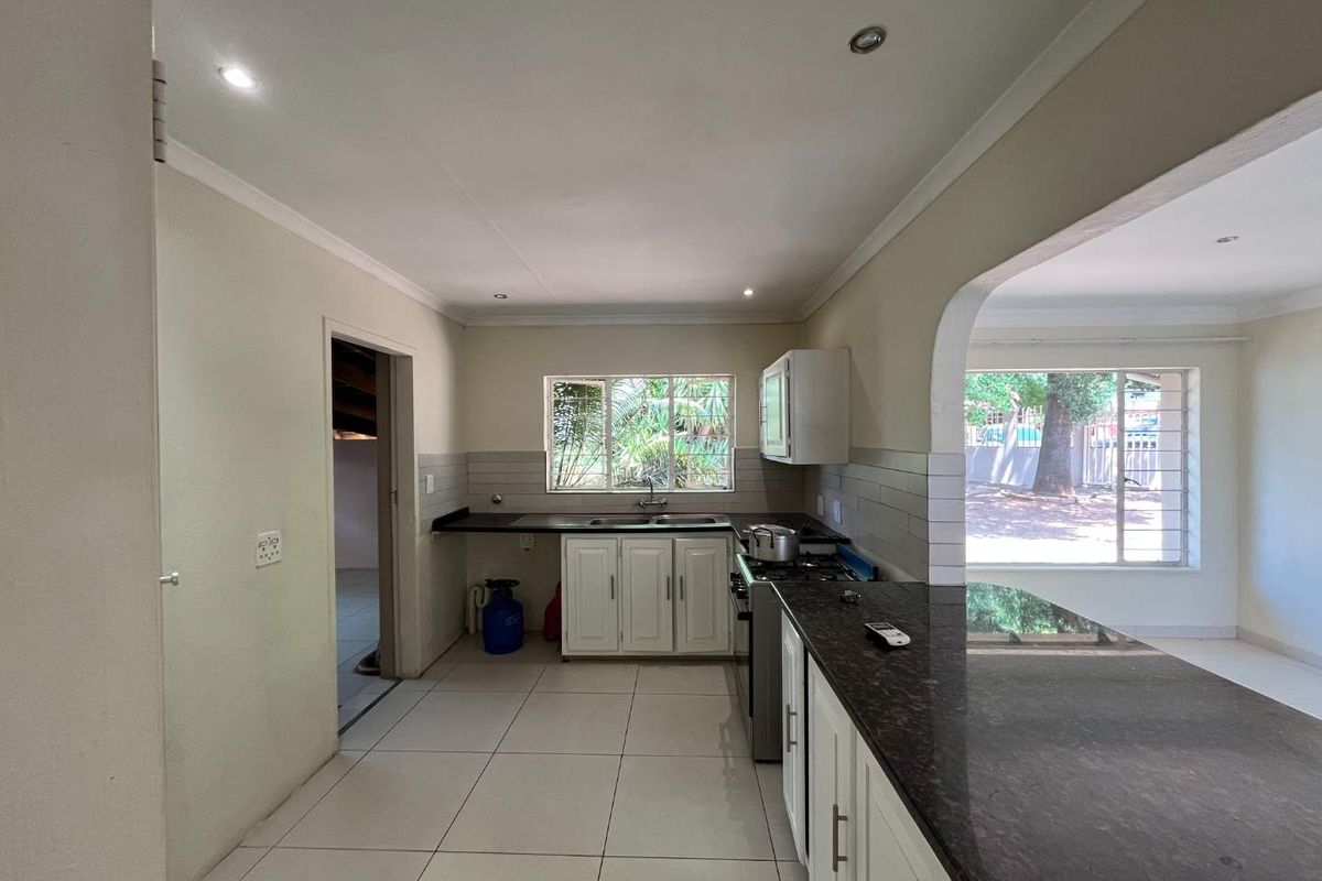 A functional kitchen featuring granite countertops, white cabinetry, a gas stove, and a breakfast bar, with tiled flooring and natural light.