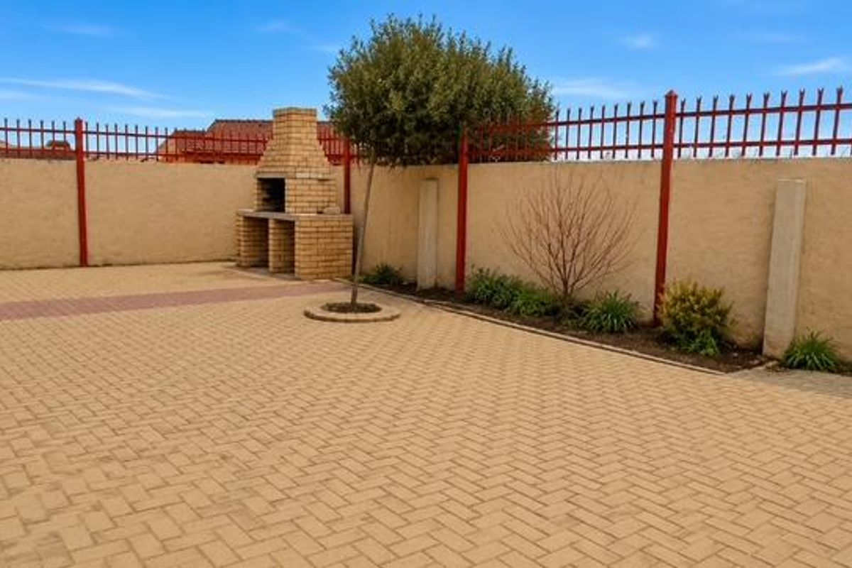 A spacious paved rear courtyard featuring a built-in brick braai, enclosed by high perimeter walls with integrated security fencing.