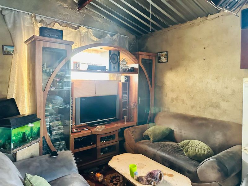 A living room area featuring exposed wall finishes and a corrugated metal ceiling, requiring significant renovation and cosmetic updates.