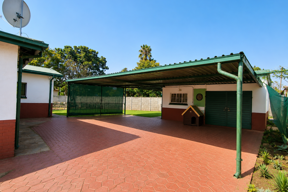 Spacious rear exterior area featuring a large covered carport, paved driveway, and secure perimeter walling.