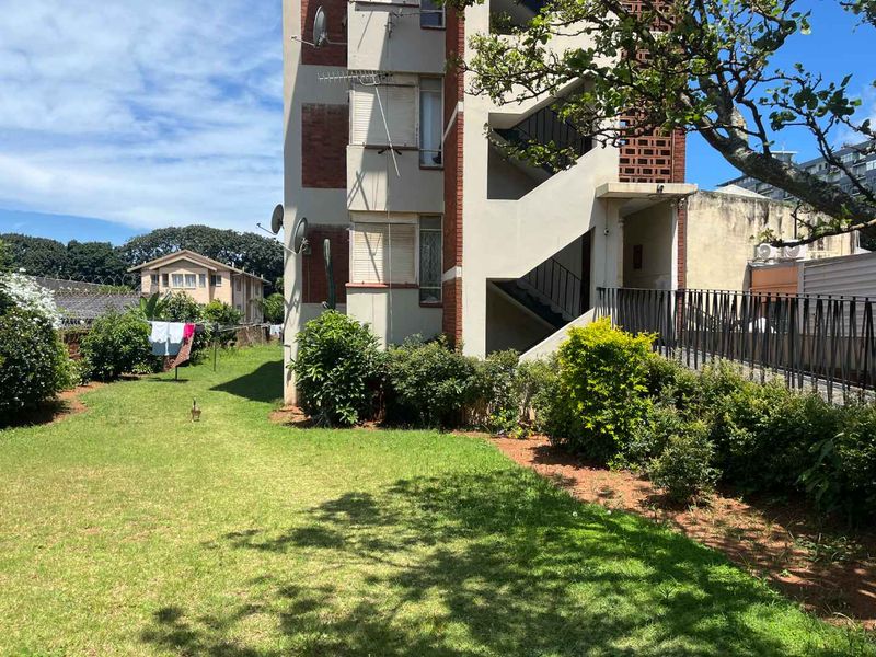 Rear view of the apartment building showing the brick facade, external staircase, and communal garden area.