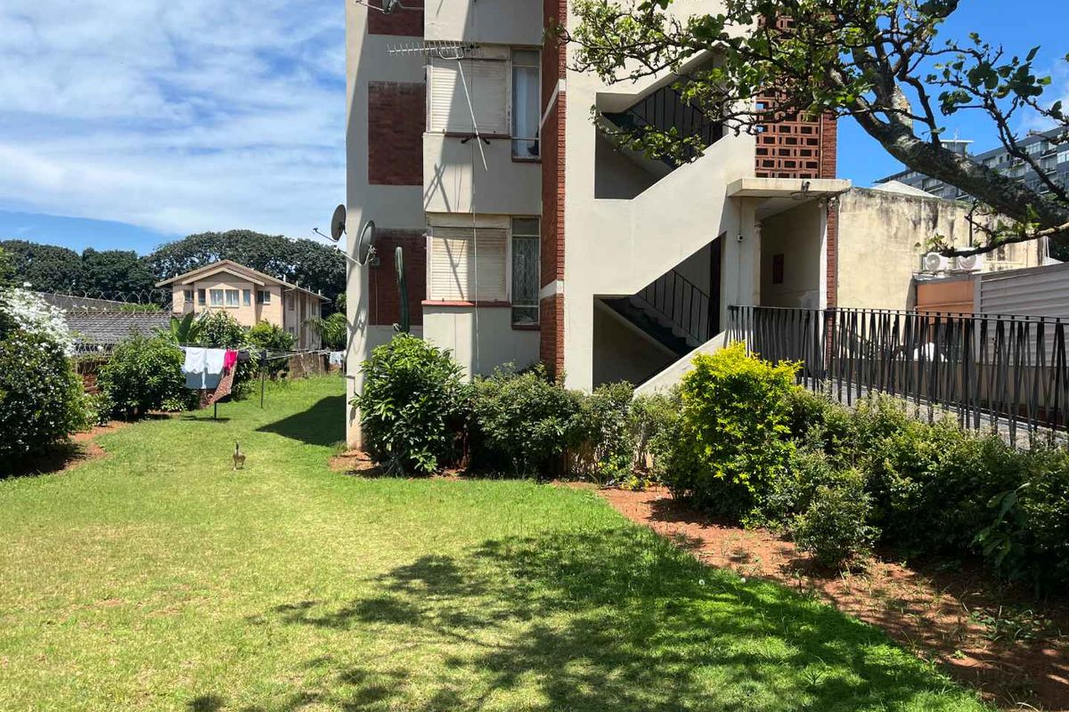 Rear view of the apartment building showing the brick facade, external staircase, and communal garden area.