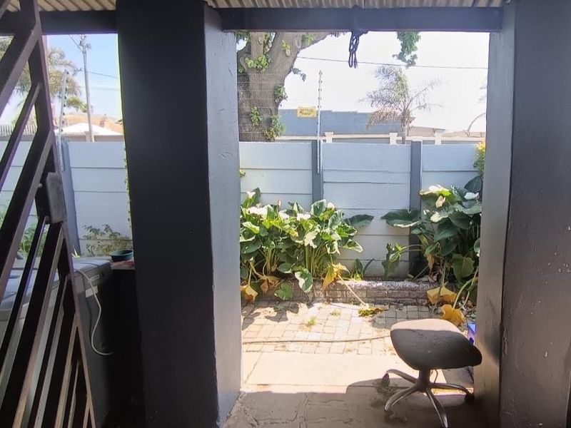 A covered outdoor patio area featuring concrete pillars, paved flooring, and a view of the rear garden with a precast boundary wall.
