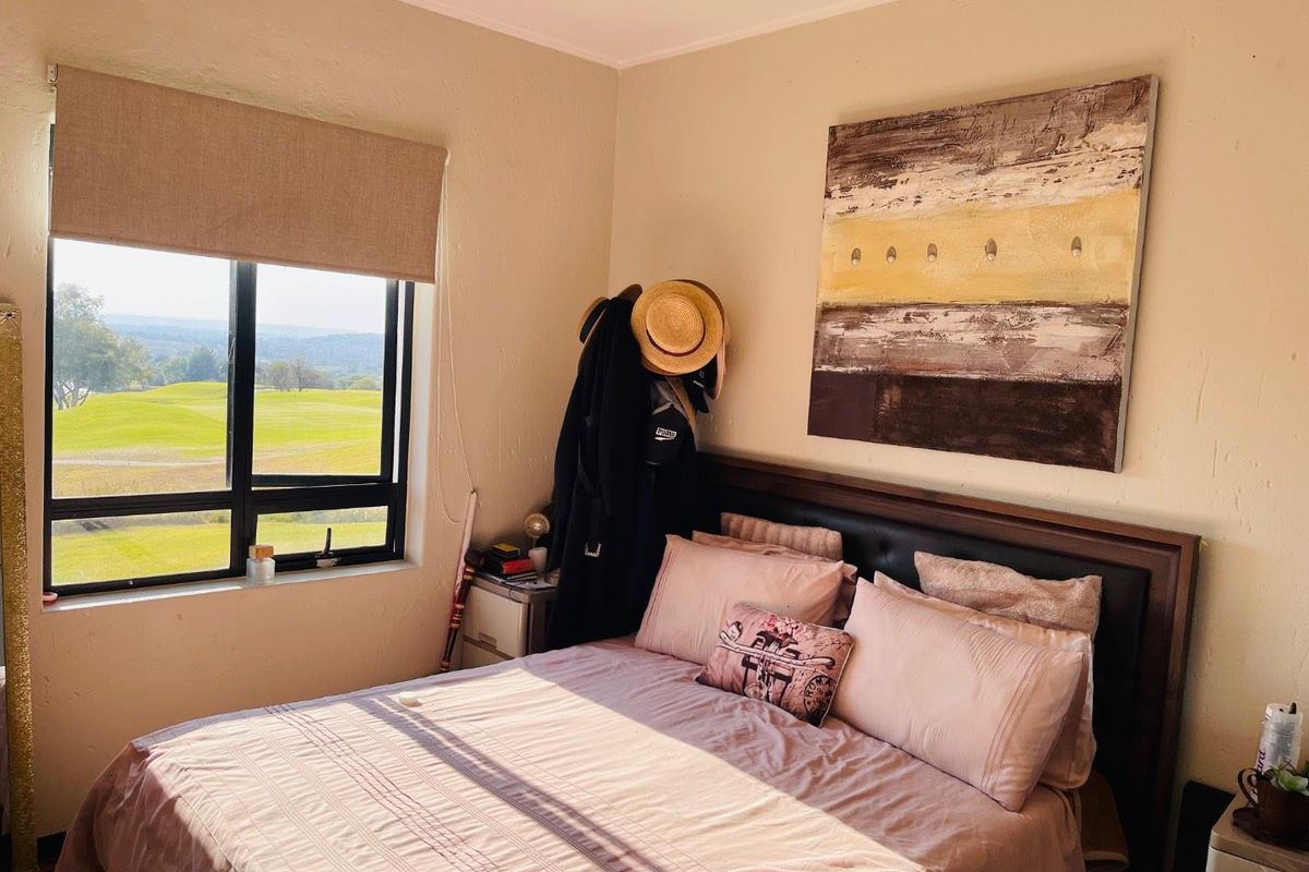 A bedroom featuring a large window with views of the surrounding landscape, neutral wall finishes, and a built-in window blind.