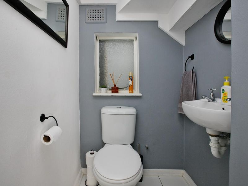 A compact, well-maintained bathroom featuring a modern toilet, wall-mounted basin, and an obscured glass window for privacy.