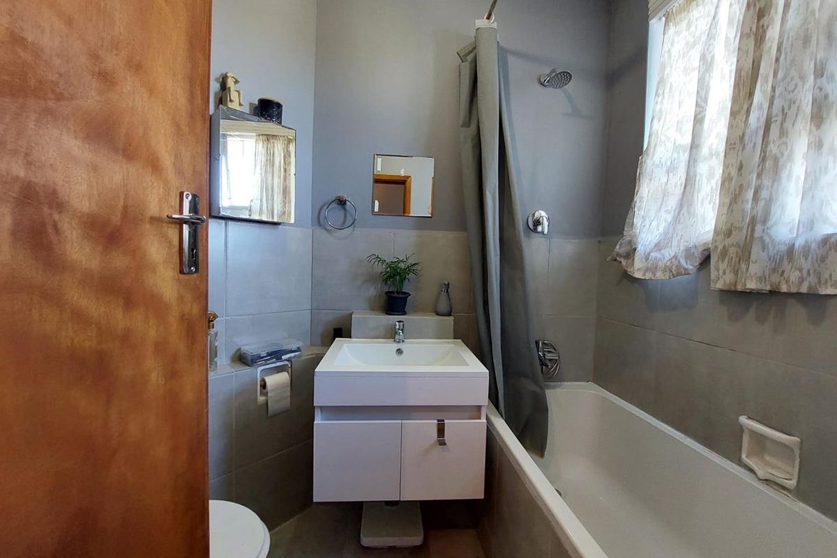 A compact bathroom featuring a wall-mounted vanity, a bathtub with a shower head, and neutral wall tiling.