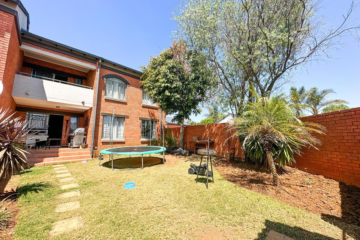 Rear view of the townhouse featuring a private garden, brick boundary walls, and a paved patio area leading to the main living space.