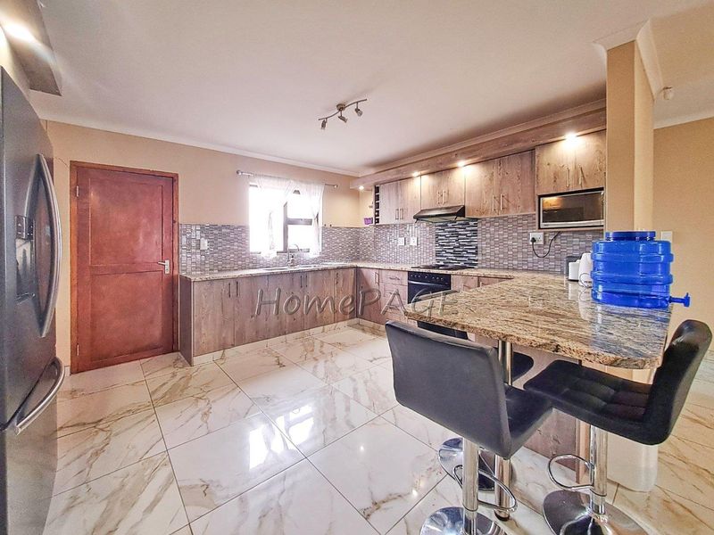 Modern kitchen featuring granite countertops, mosaic tile backsplash, built-in cabinetry, and high-quality tiled flooring with a breakfast bar area.