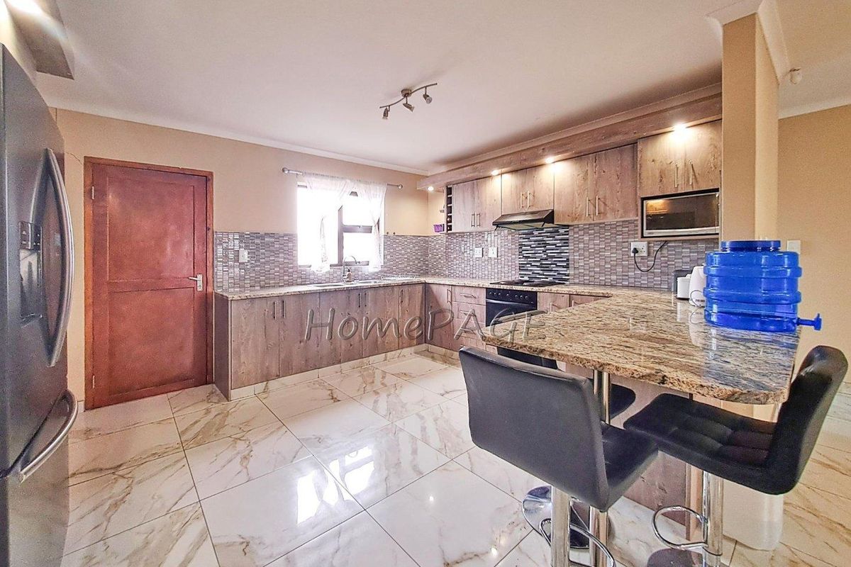 Modern kitchen featuring granite countertops, mosaic tile backsplash, built-in cabinetry, and high-quality tiled flooring with a breakfast bar area.