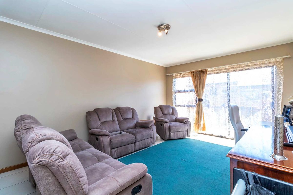 A spacious living room featuring large windows that provide ample natural light, neutral wall tones, and tiled flooring.
