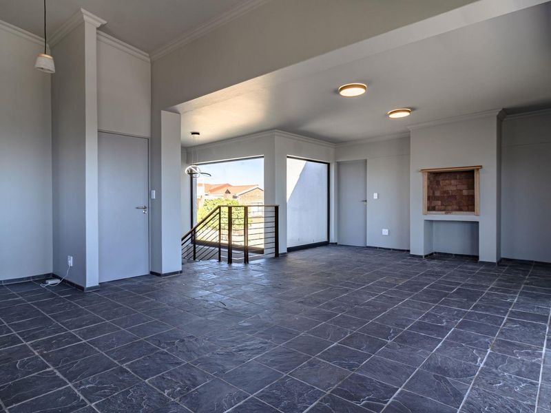 Spacious open-plan living area featuring dark slate tile flooring, a built-in fireplace, and large windows providing natural light and access to the staircase.