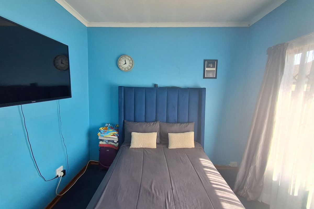 A standard bedroom featuring blue painted walls, dark carpeting, and a window with curtains.