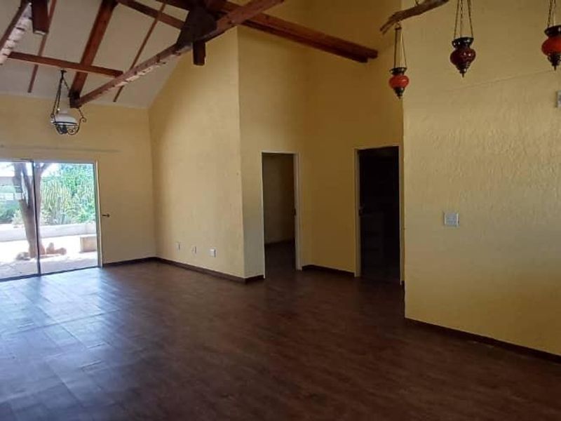 Spacious living area featuring vaulted ceilings with exposed timber beams, laminate flooring, and a sliding glass door providing access to the exterior.