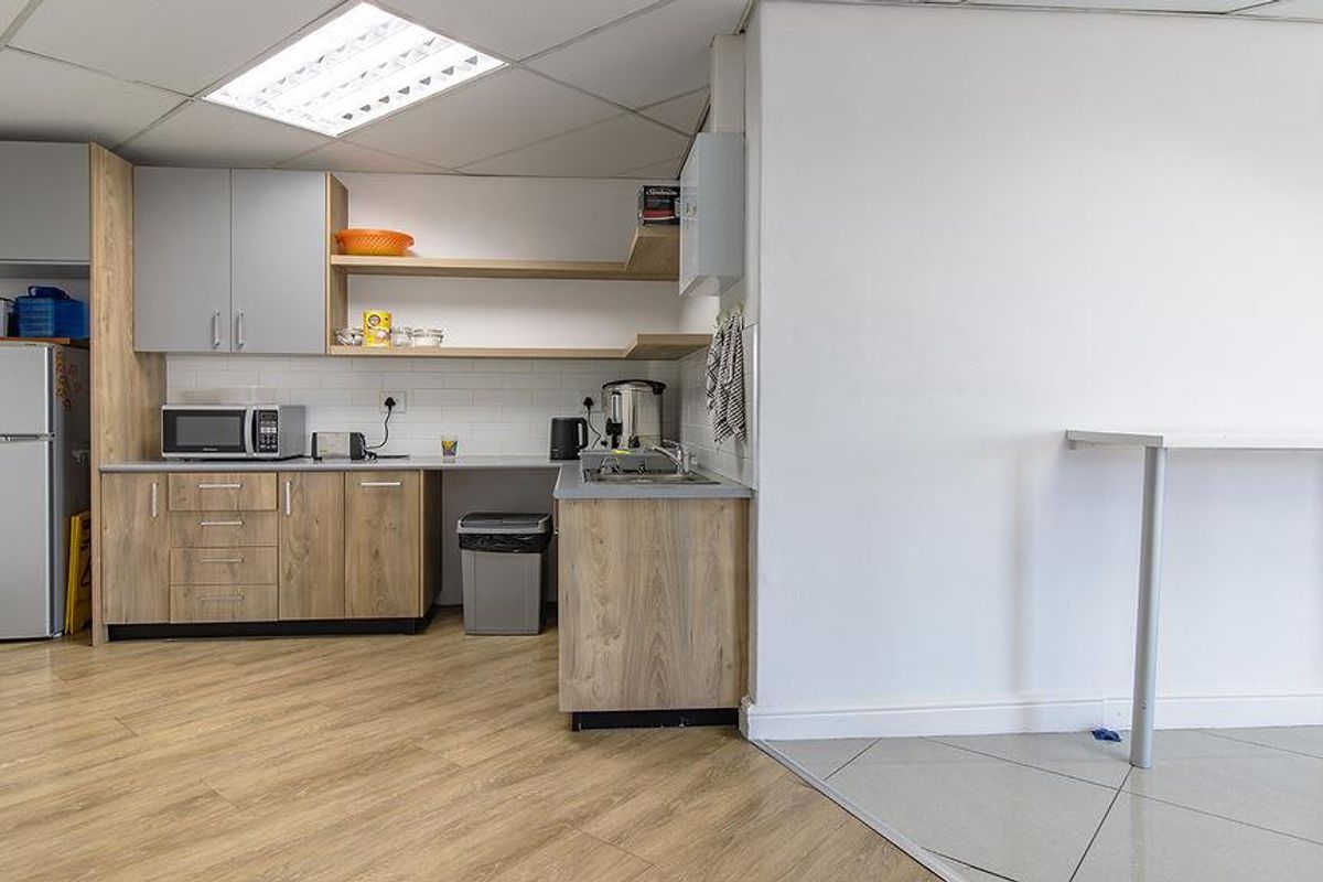 A functional office kitchenette featuring wood-look cabinetry, a stainless steel sink, and integrated shelving, adjacent to a tiled workspace area.