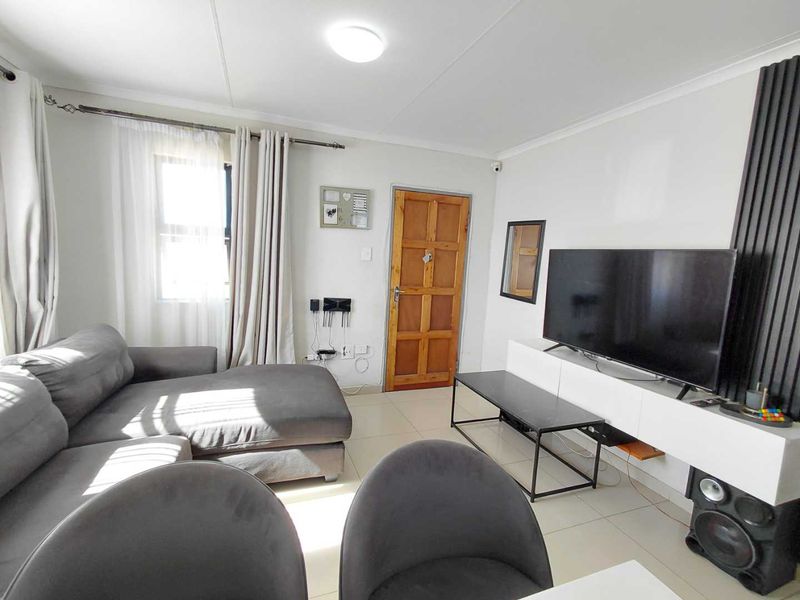 A bright living room featuring tiled flooring, a wooden panel door, and a modern slatted wall feature for media placement.