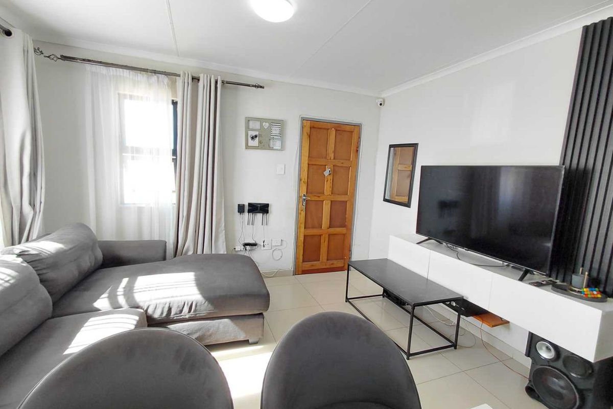 A bright living room featuring tiled flooring, a wooden panel door, and a modern slatted wall feature for media placement.