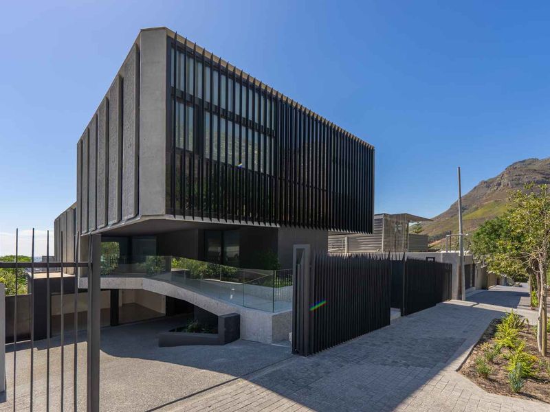 Modern architectural house exterior featuring concrete construction, vertical metal screening, and a sleek driveway entrance with glass balustrades.