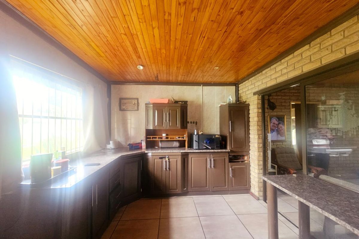 A functional kitchen featuring dark cabinetry, tiled flooring, and a timber-paneled ceiling, with a breakfast bar area adjacent to the living space.
