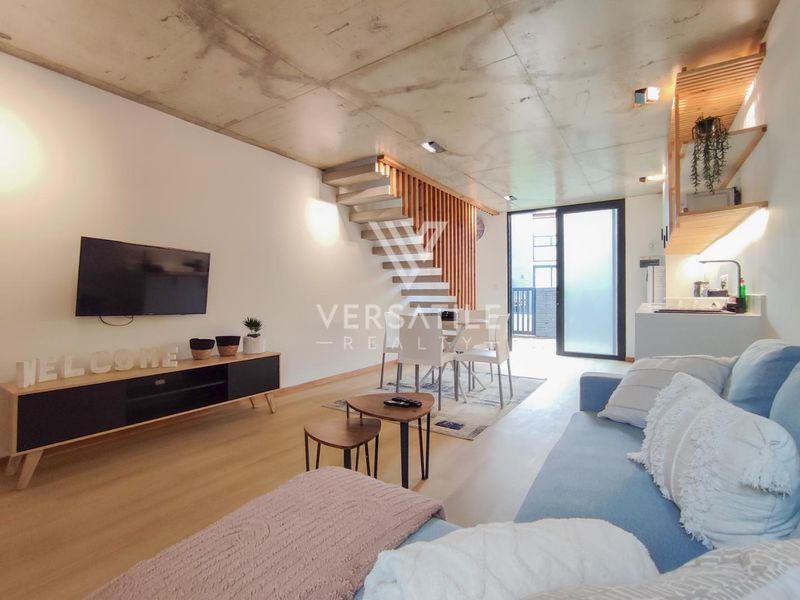 Modern open-plan living area featuring an exposed concrete ceiling, timber staircase with slat screen, and seamless access to the outdoor space.