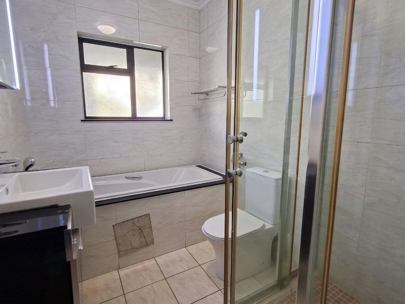 A clean, modern bathroom featuring a built-in bathtub, separate glass-enclosed shower, toilet, and wall-mounted basin with neutral tiled finishes.