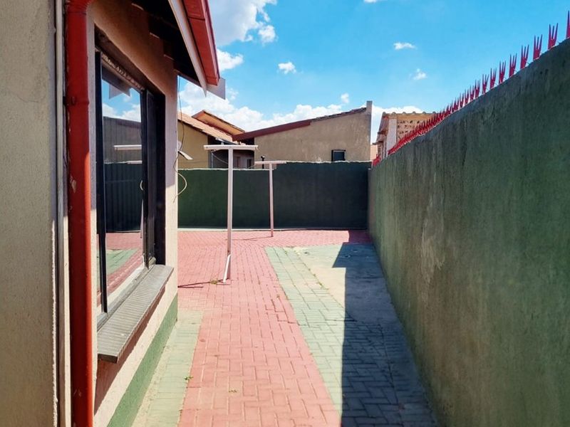 A side exterior view of the property featuring a paved walkway, boundary wall with security spikes, and functional guttering system.