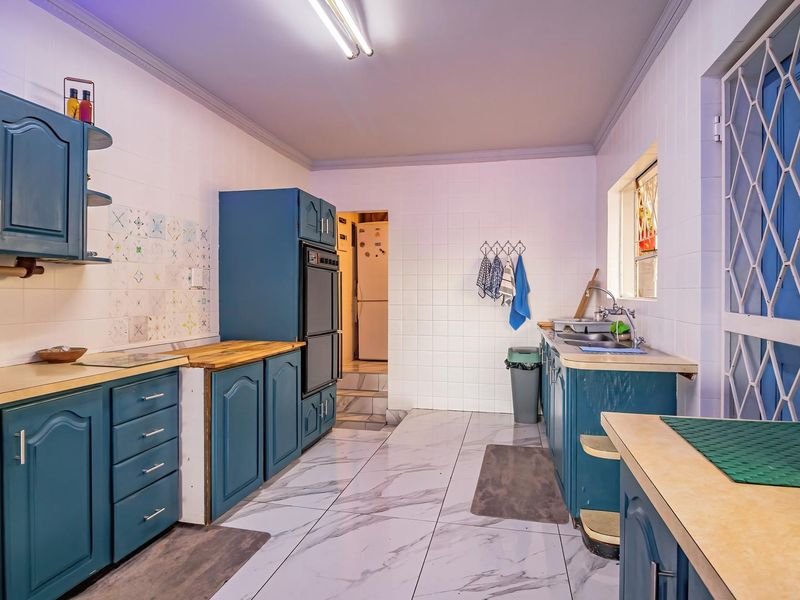 A functional kitchen featuring blue cabinetry, a double wall oven, tiled walls, and marble-look floor tiles with a security gate leading to the exterior.