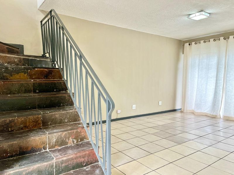 An empty living area featuring a tiled staircase with a metal balustrade, ceramic floor tiles, and access to a sliding glass door.