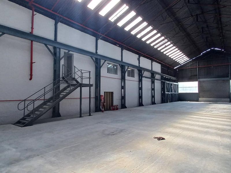 Spacious industrial warehouse featuring a high-clearance steel portal frame, polished concrete flooring, integrated skylights, and a functional metal staircase for mezzanine access.