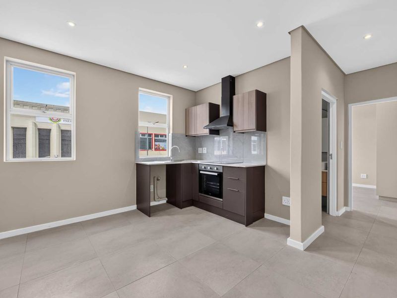 Modern kitchen featuring dark cabinetry, built-in oven and hob, extractor fan, and neutral tiled flooring in an open-plan layout.