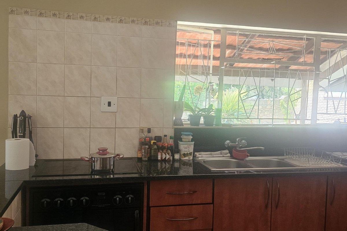 Kitchen featuring dark granite countertops, wooden cabinetry, a built-in electric hob, and a double-basin sink with a window view.