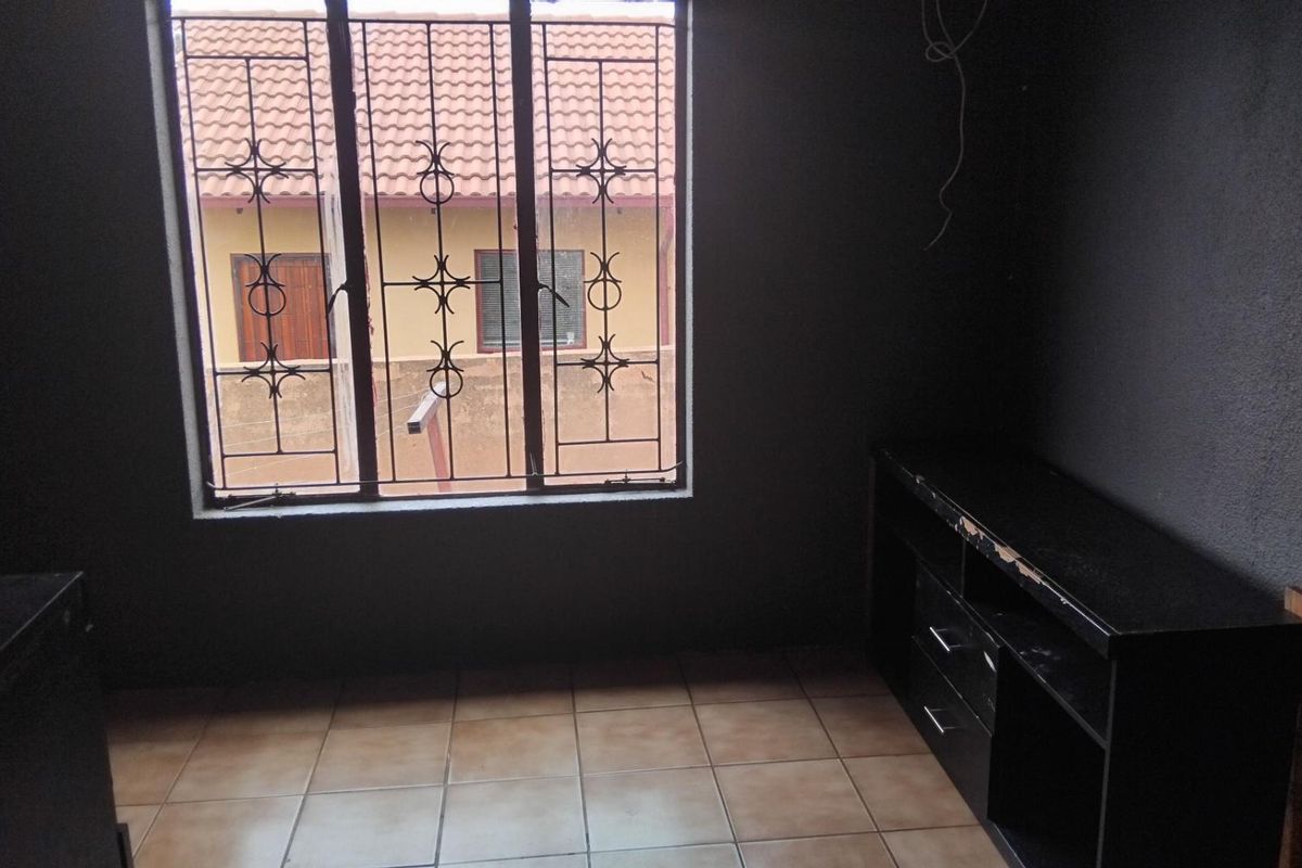 A bedroom featuring dark painted walls, tiled flooring, and a window fitted with security burglar bars.