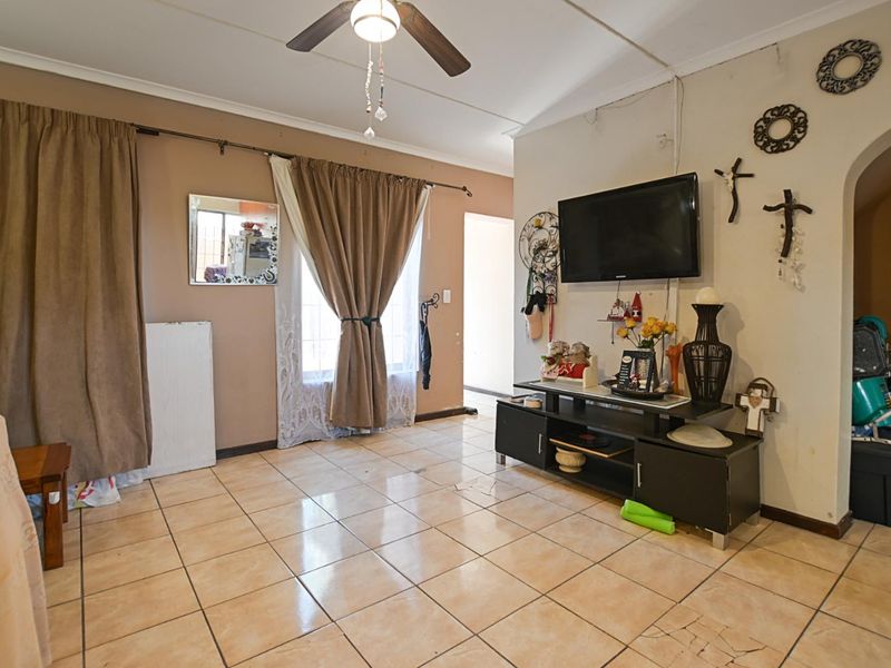 A living room featuring ceramic floor tiles, a ceiling fan, and an arched entryway, showing signs of wear and exposed electrical wiring.