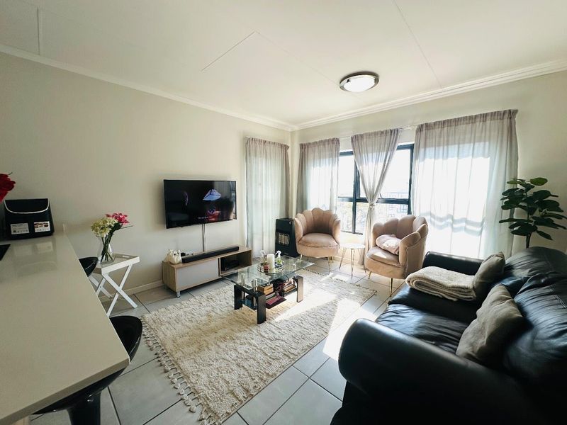 A bright and comfortable living room featuring tiled flooring, a large window with natural light, and a neutral color palette.