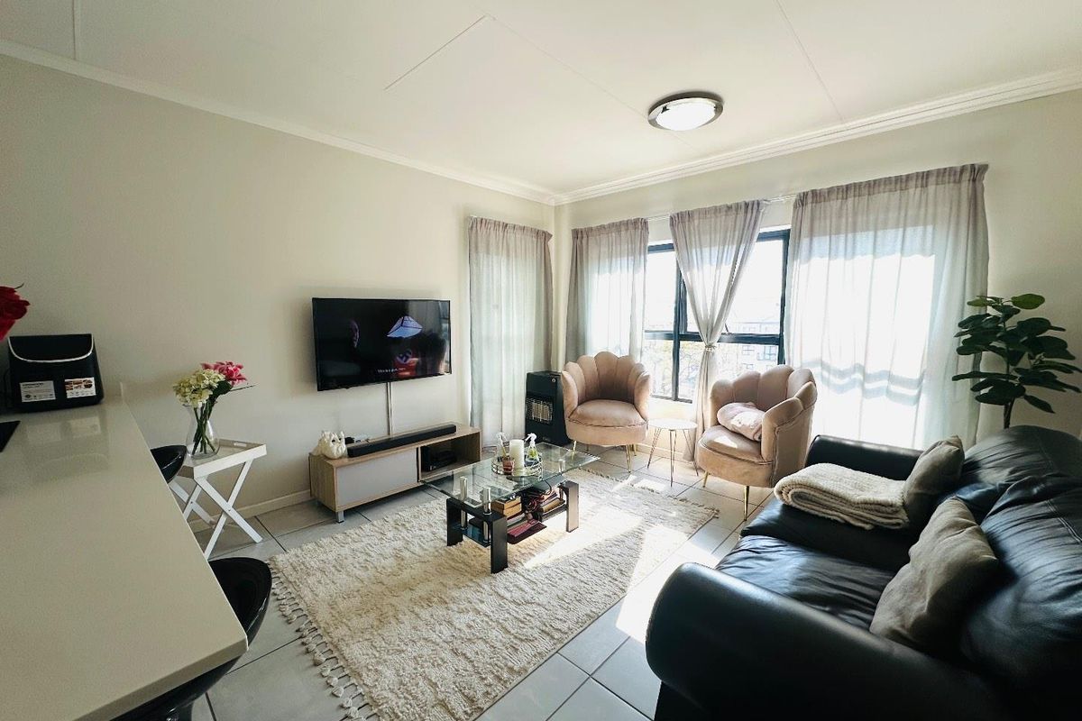 A bright and comfortable living room featuring tiled flooring, a large window with natural light, and a neutral color palette.