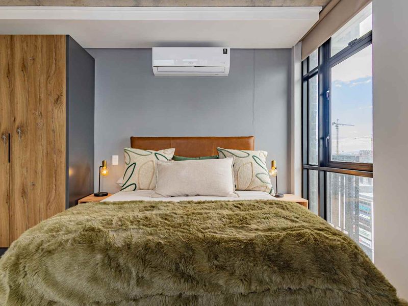 Modern bedroom featuring a built-in wardrobe, split-system air conditioning, and large windows with natural light and an exposed concrete ceiling finish.