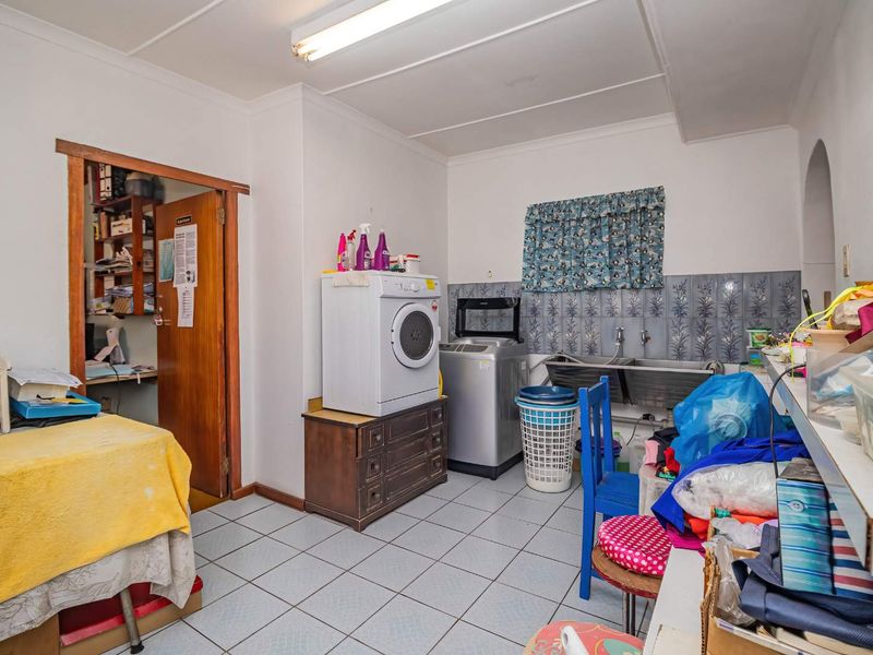 A functional laundry room featuring a double stainless steel sink, tiled flooring, and tiled splashback, offering practical utility space for the home.
