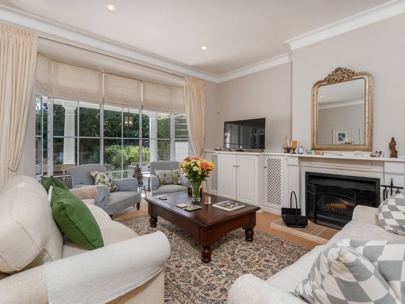 A bright and inviting living room featuring a classic fireplace, custom built-in cabinetry, and large bay windows that provide ample natural light and garden views.