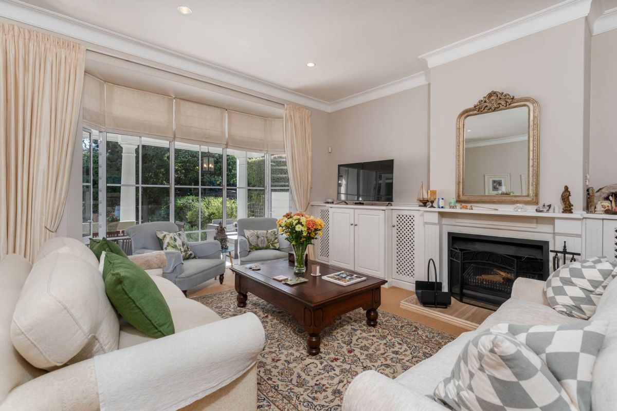 A bright and inviting living room featuring a classic fireplace, custom built-in cabinetry, and large bay windows that provide ample natural light and garden views.